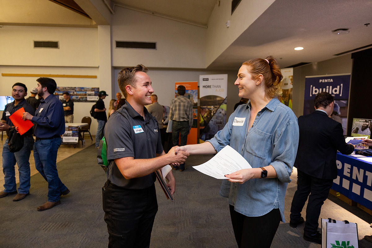 A student shakes hands with a recruiter at a career fair.