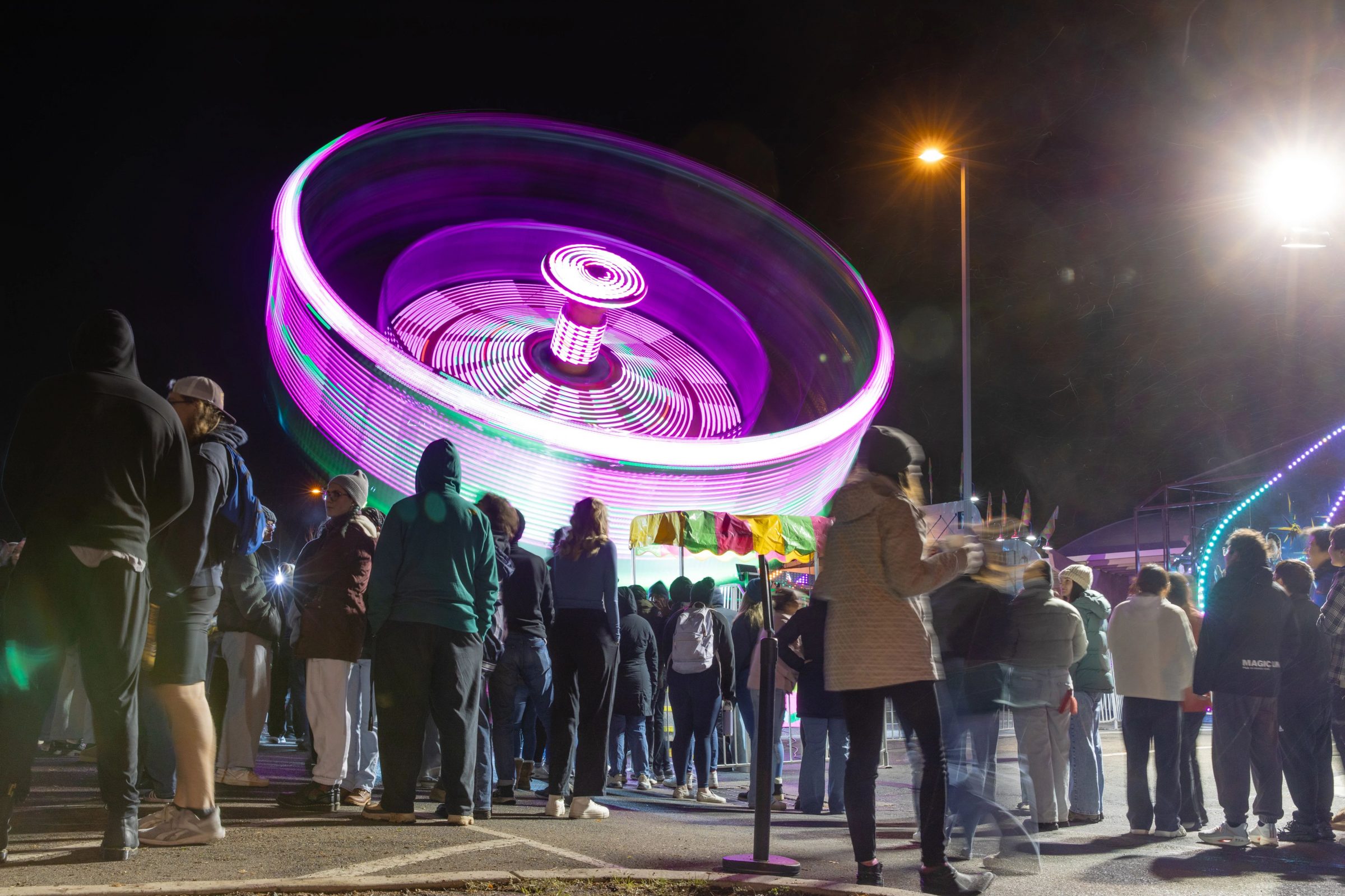 Students wait in line to ride a spinning, glowing carnival ride at the Homecoming Carnival.