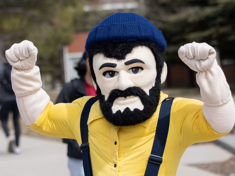 Louie the Lumberjack stands near the bike path at NAU in a victory stance—with his fists up in the air.