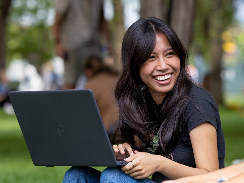 Two students laugh while working on a laptop outside.