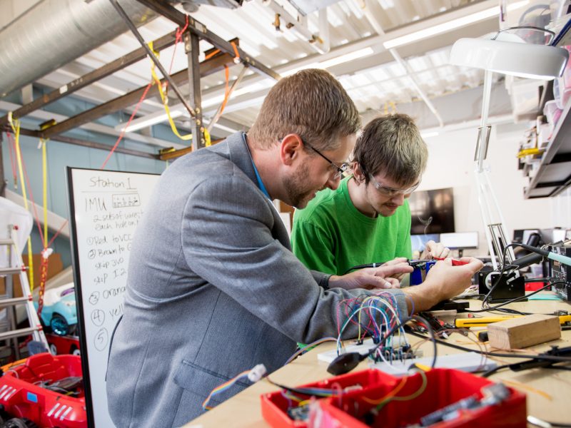 Researcher and student researcher working at workbench in lab on software and hardware technology.
