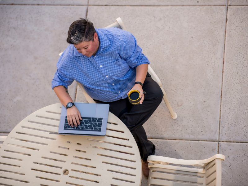 A photo of a man sitting and working on his computer with a cup of coffee.