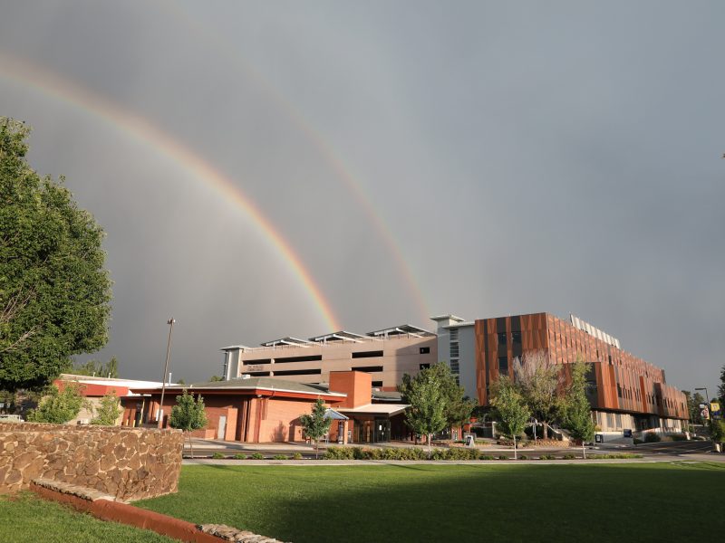 Rainbow against a dark gray sky over campus buildings.