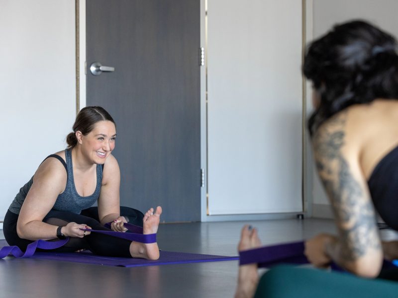 Yoga student smiling as she using a band to stretch on the ground.