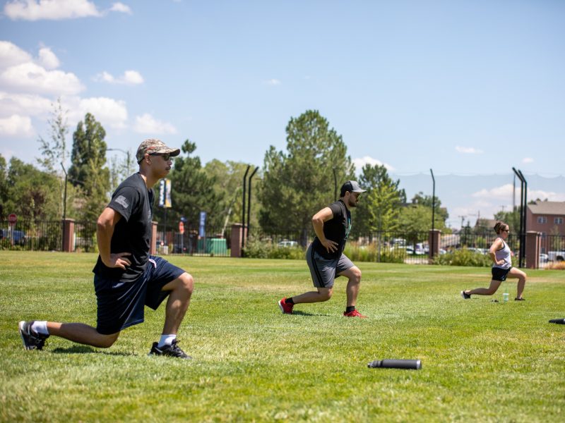Three people on a field participating in lunging stretching exercises.