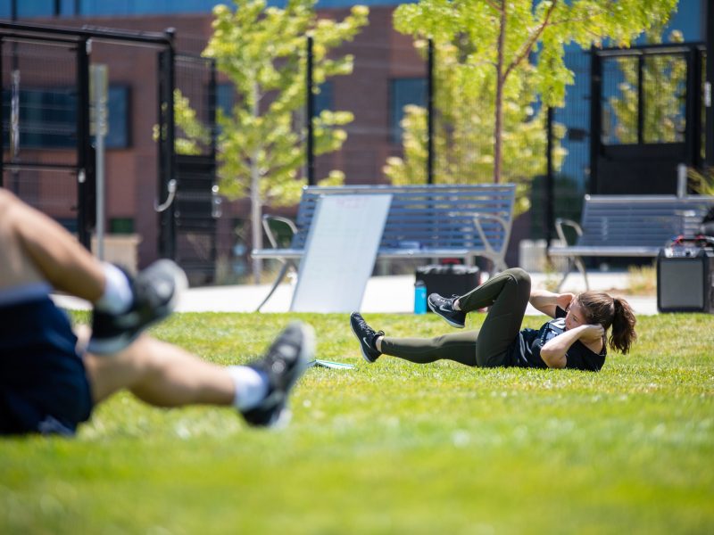 Female student laying on the grass working out.