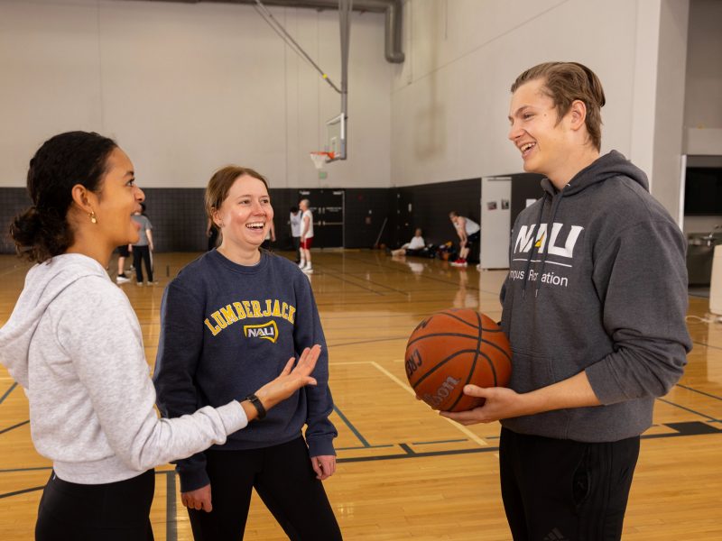 Two female students talking to a student holding a basketball.