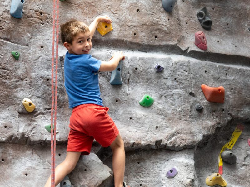 A male kid looking back and smiling on a bouldering rock.