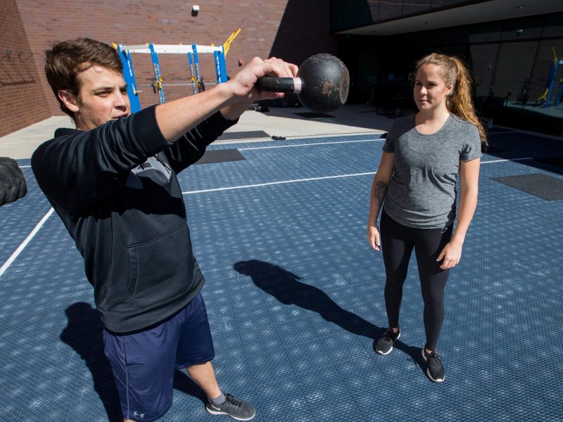 One student swinging kettlebell while other student watched.