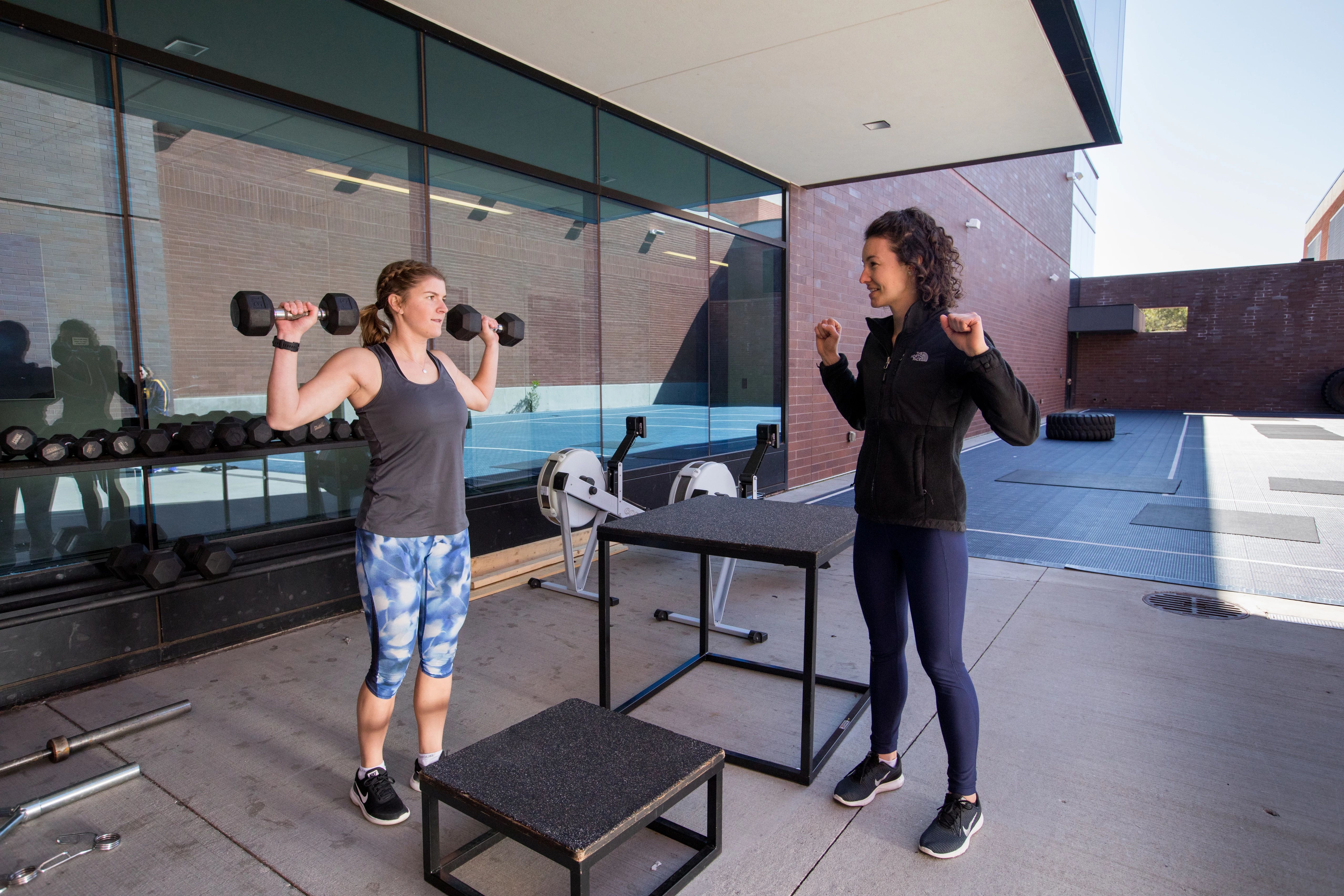Trainer helping student with weight-lifting workout outside of campus recreation building.