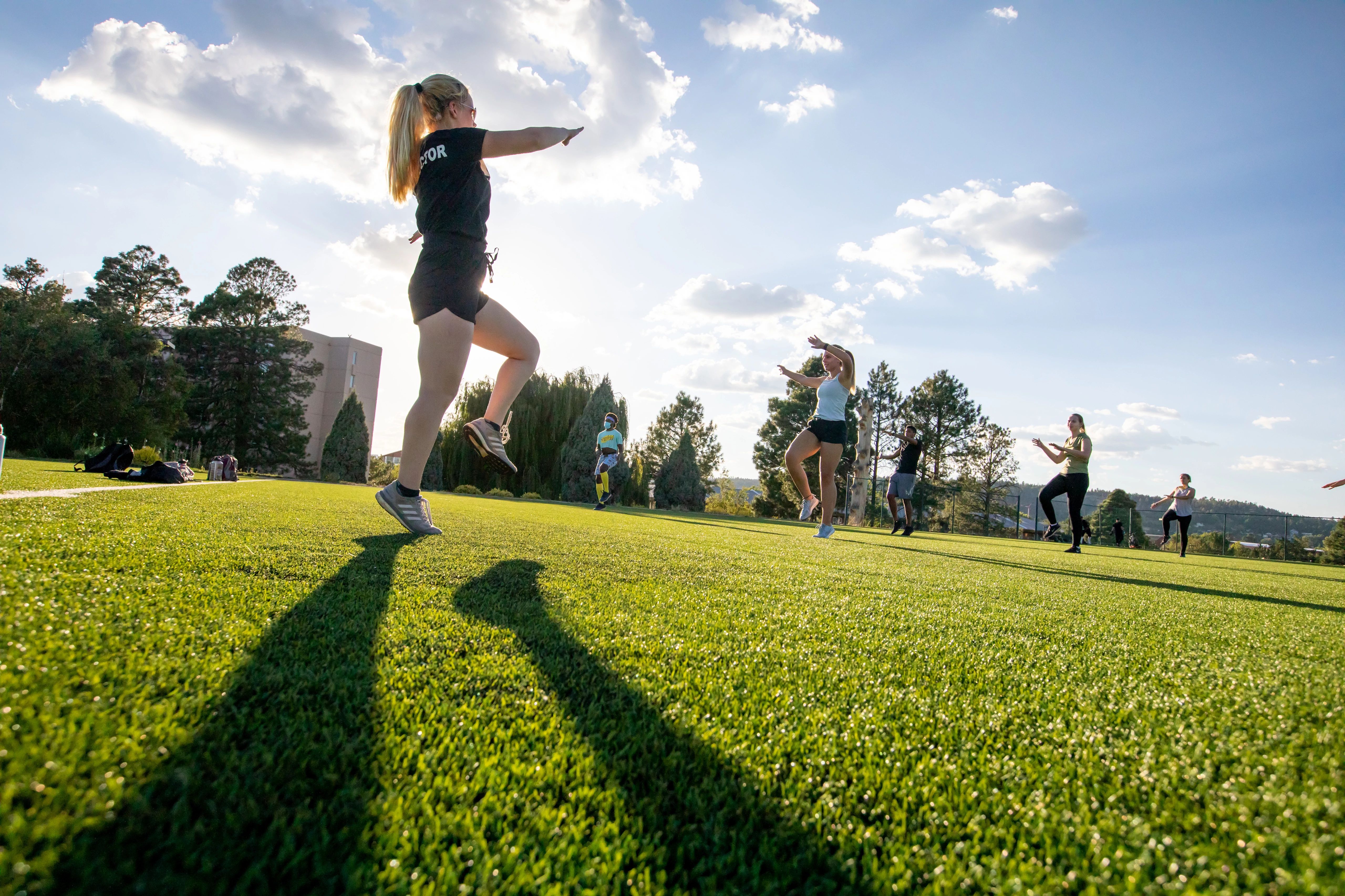 Group fitness class on campus lawn, showing woman leading doing cardio exercises.