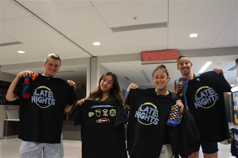 Four students holding up t-shirts and posing for the camera.