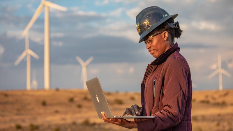 Student writing a report on a computer at a wind farm.