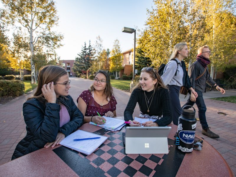 Three students collaborating together outside at a table.