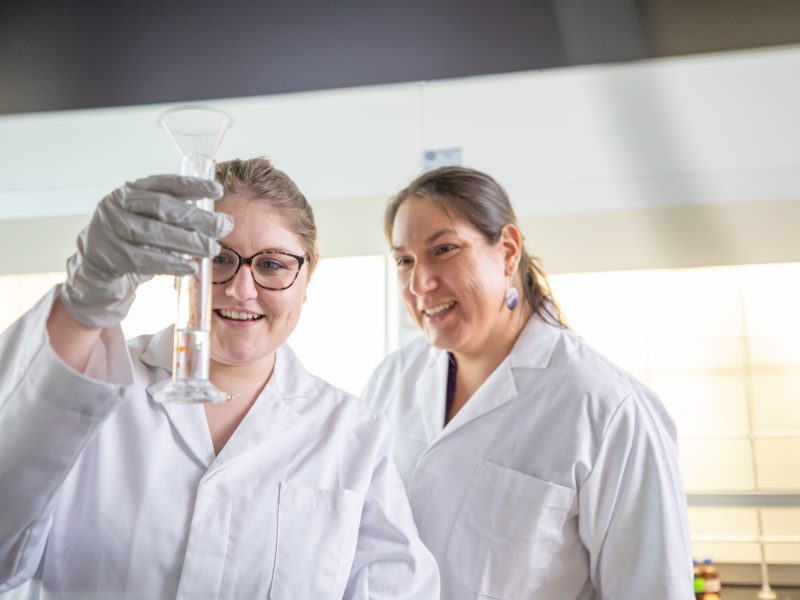 Two students looking at a glass tube for a scientific experiment.