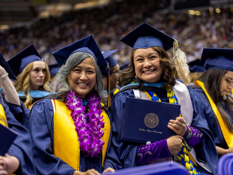 NAU students smile as they hold up their newly acquired degrees.