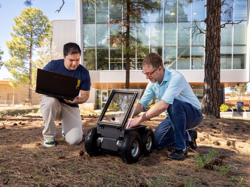 Student and instructor working on a robot on wheels outside of the engineering building.