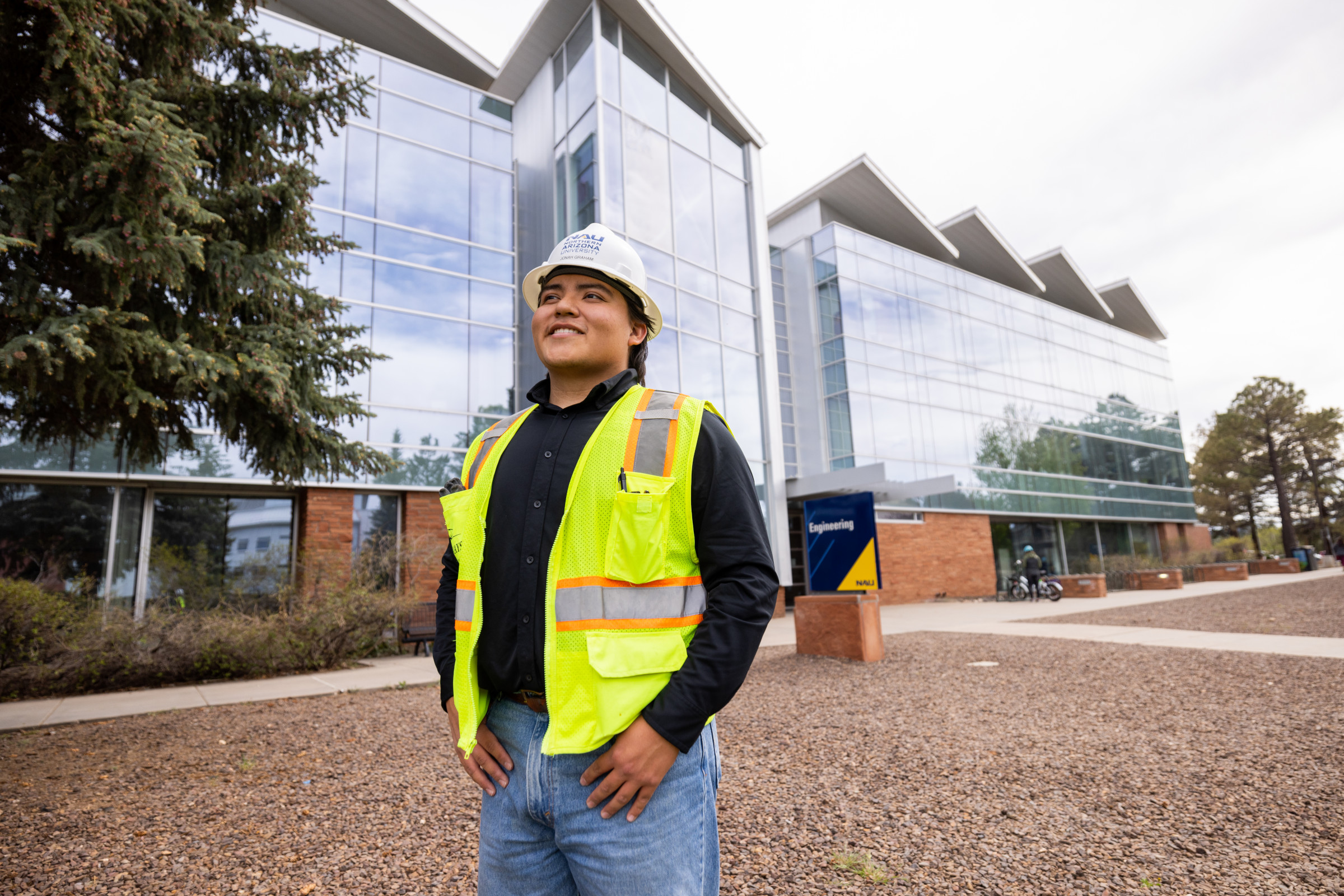 Engineering student standing outside the engineering building wearing a safety vest and hardhat.