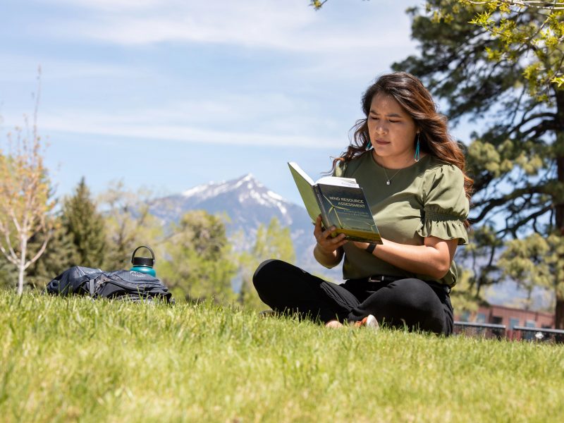 Student sitting in grass field on campus while studying her book.