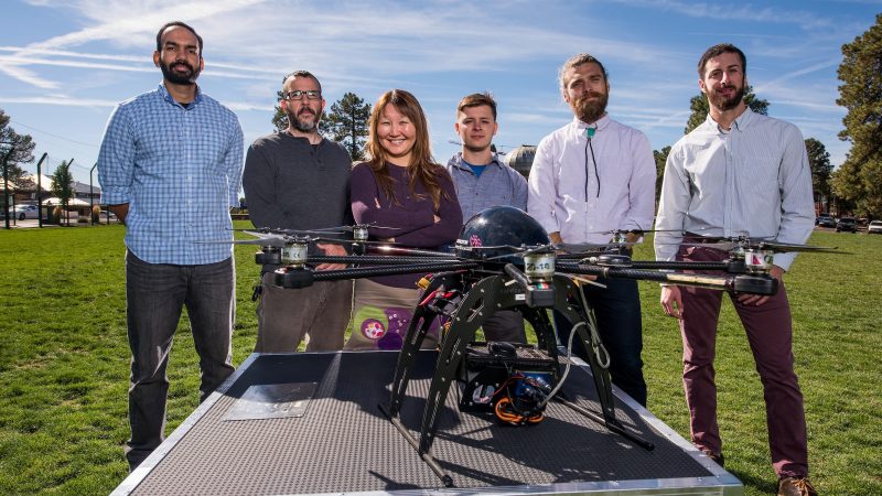 Students and professors in a grass field posing next to a large drone.