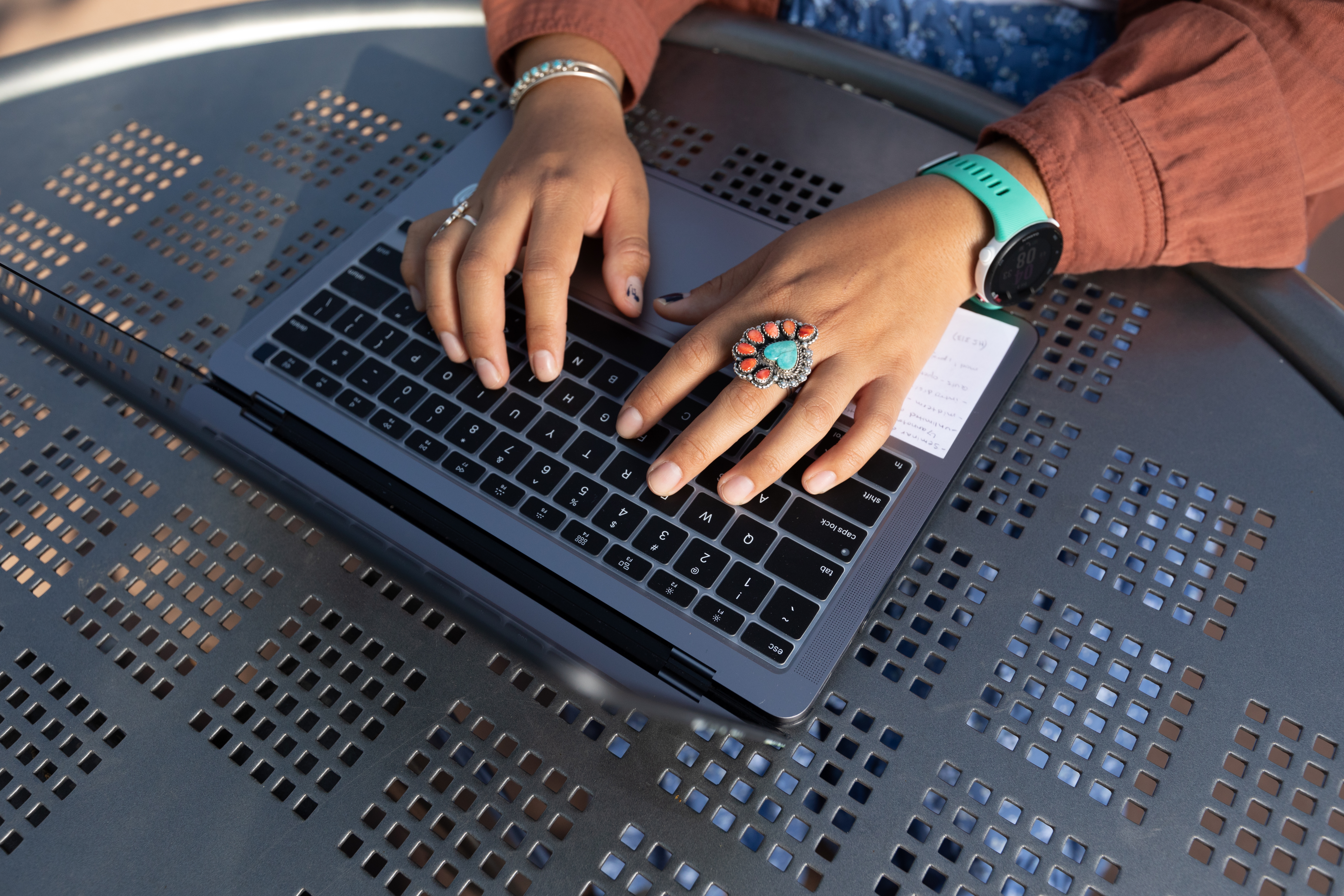 Hands with turquoise rings typing on a laptop keyboard.