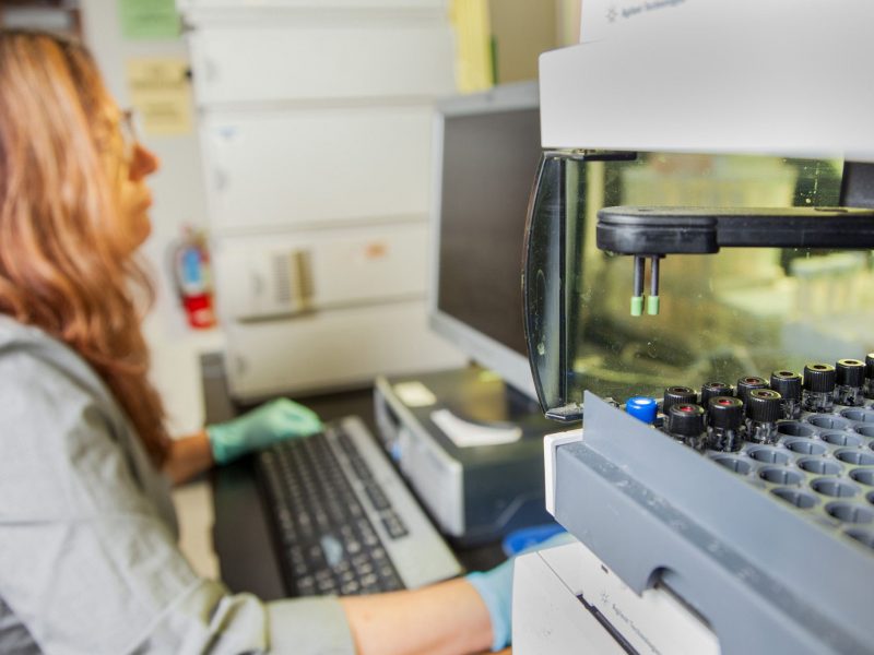 Woman working in a lab focusing on equipment on a table next to her.