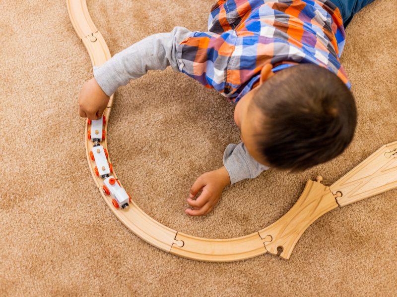 Child playing with cars on a track and laying on the floor.