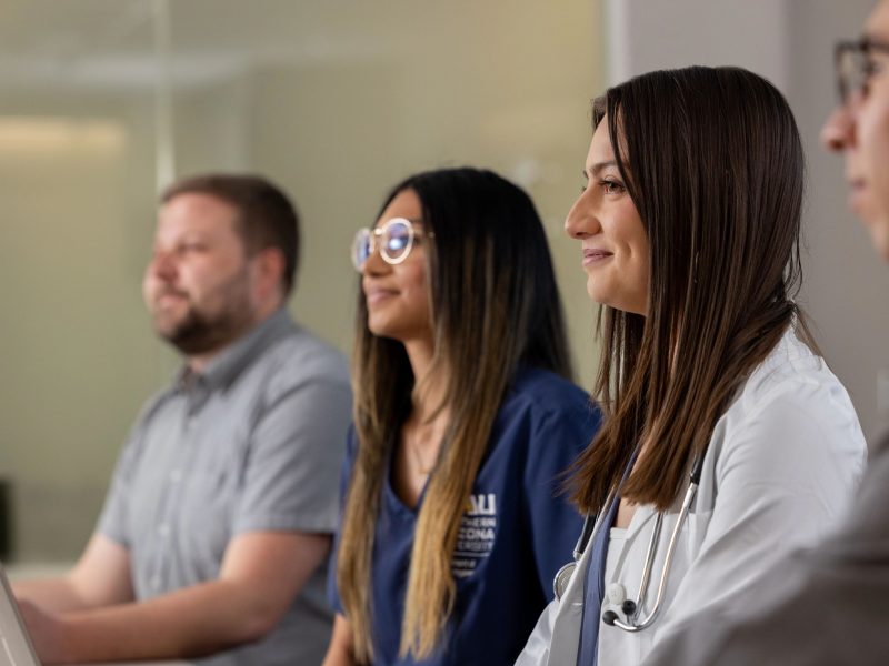 Health students sitting at a table listening to someone speaking.