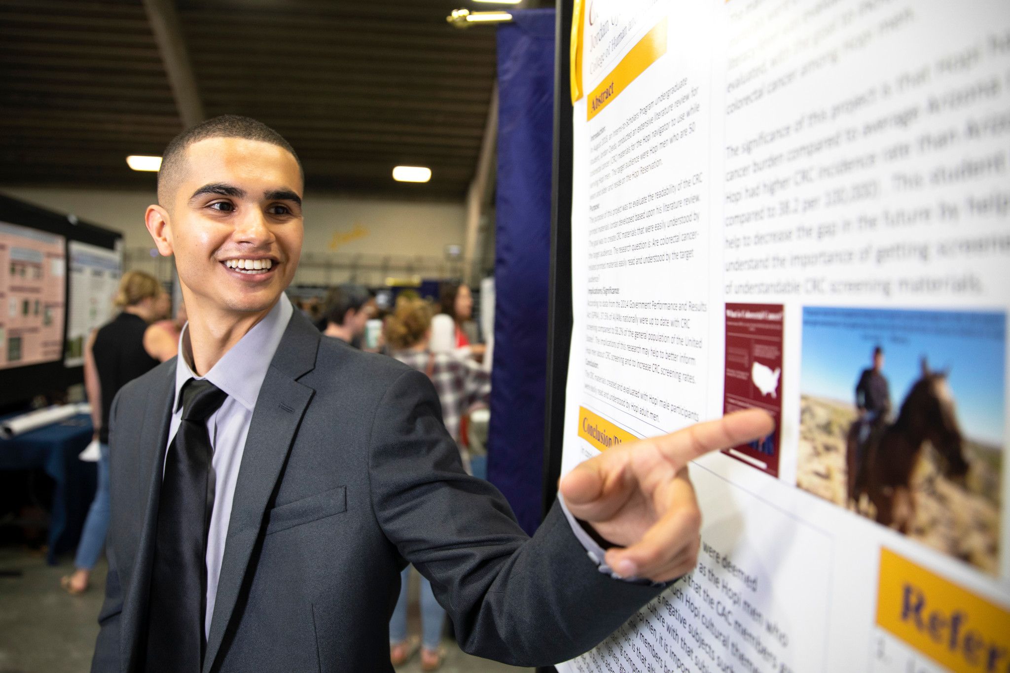 Student pointing towards his research poster at symposium.