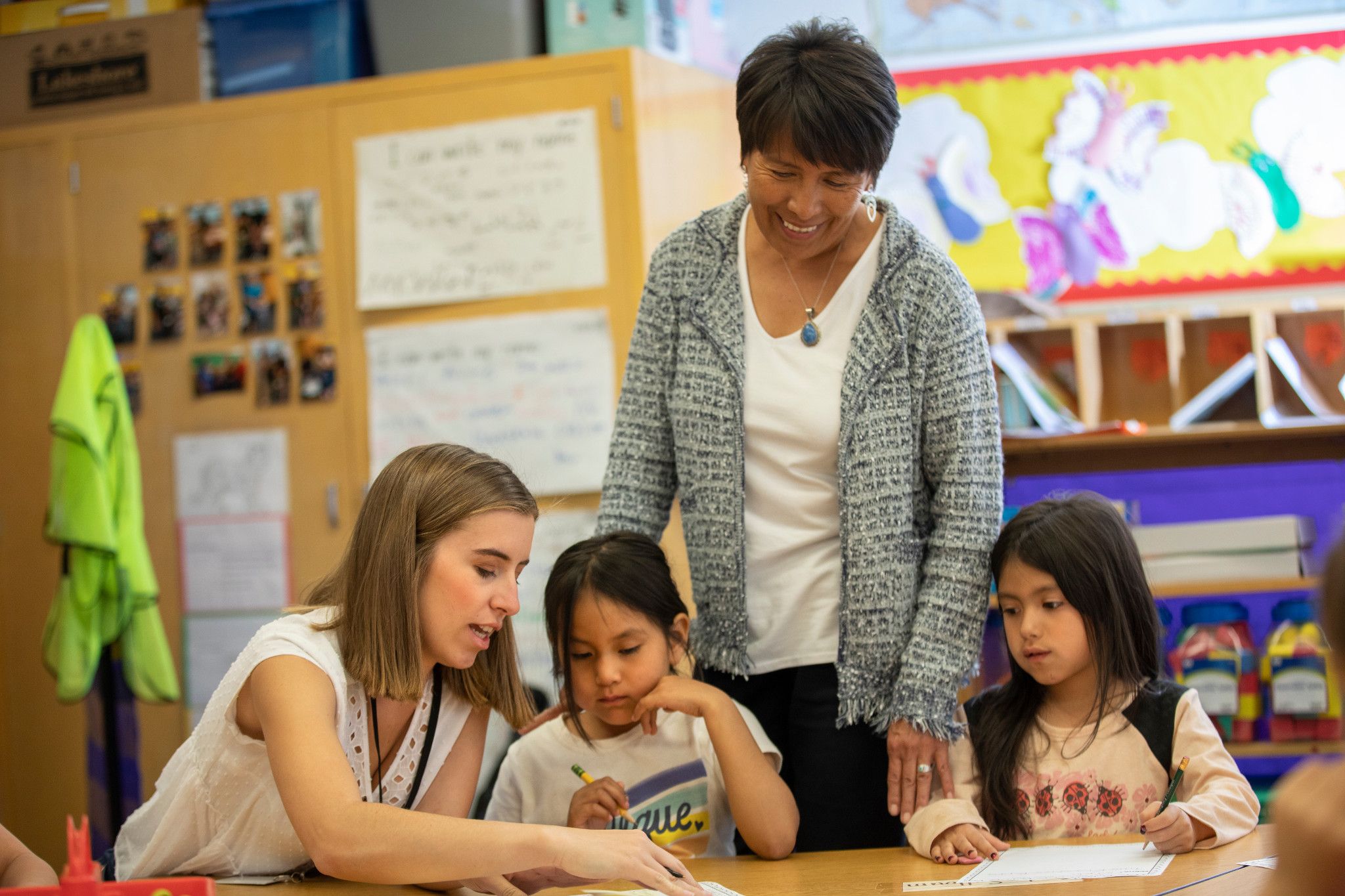 Professor watching student teacher help young kids with an assignment.