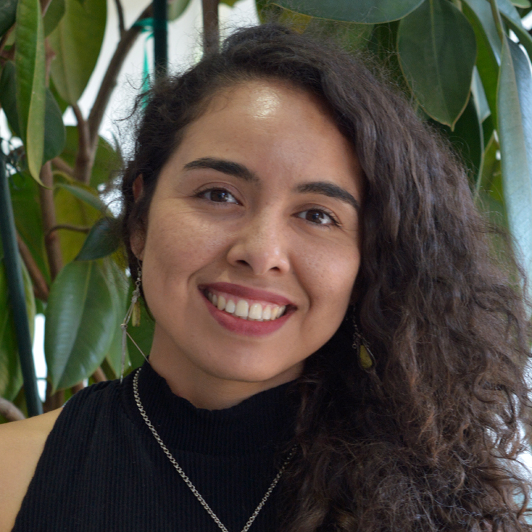 Alexandra Elvira Samarron Longorio is wearing a black top and necklace and earrings standing front of a large plant.