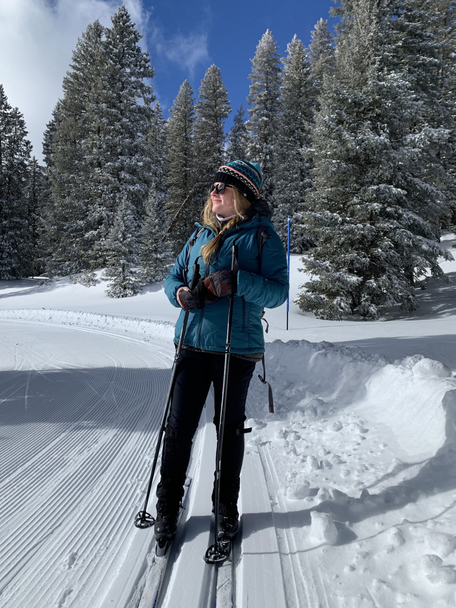 Amy Gelatt in ski cloth, hat, standing with skis on and poles in hands.