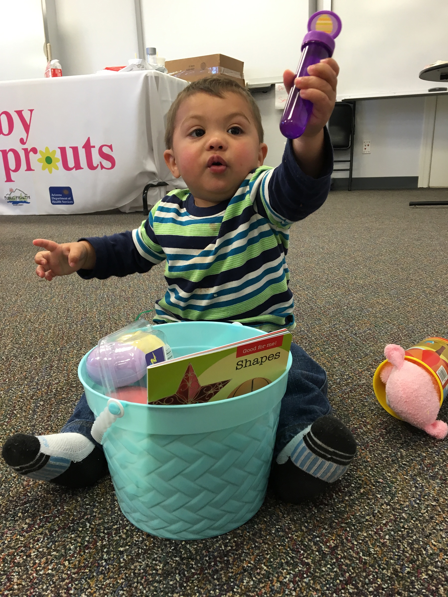 A baby sitting on floor playing with toys out of a bucket.