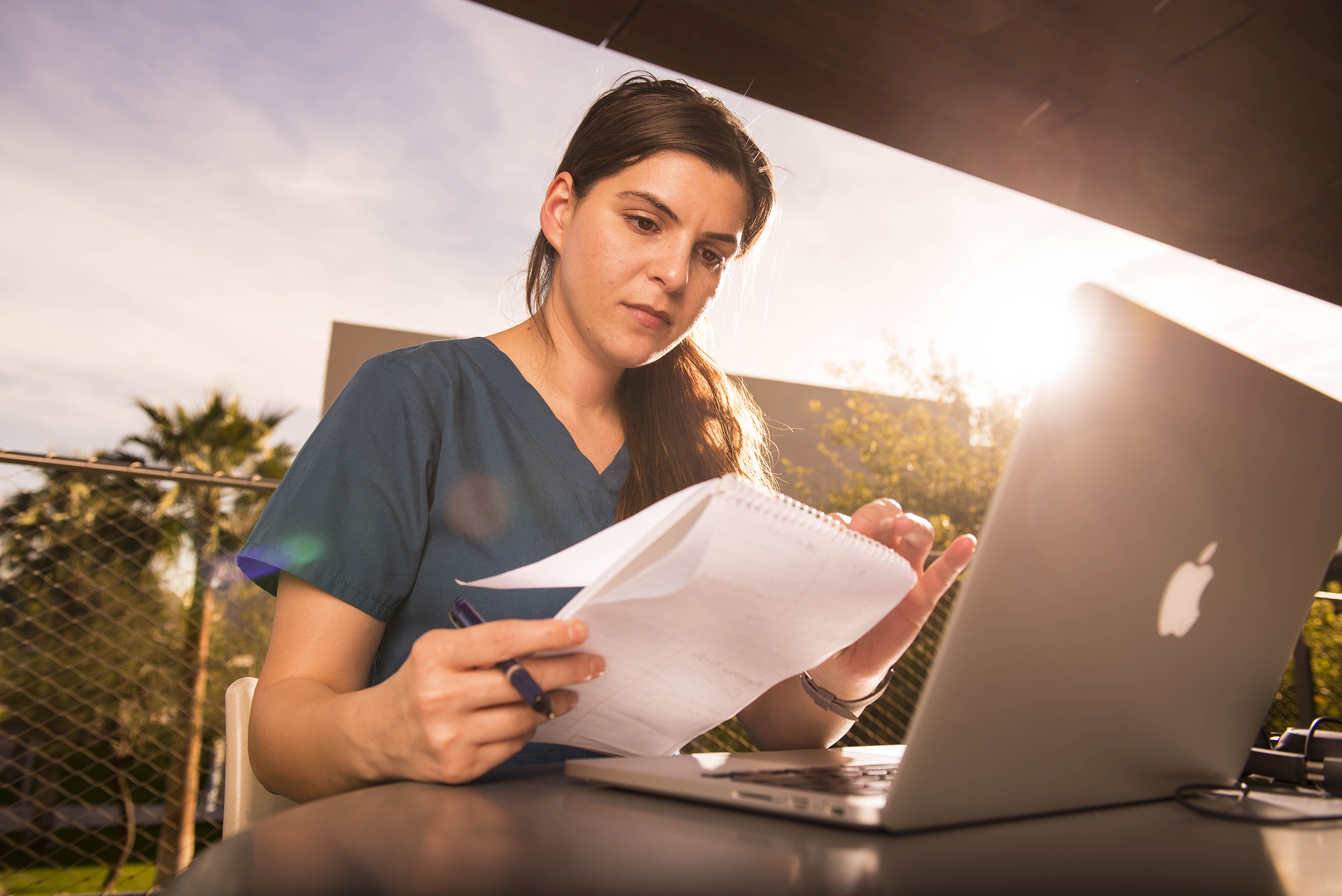 Student sitting outside working on a laptop and notes.