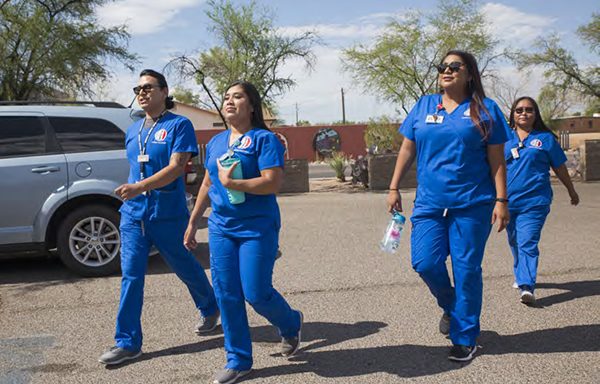 Four Community Health Workers walking outside in blue scrub uniforms.