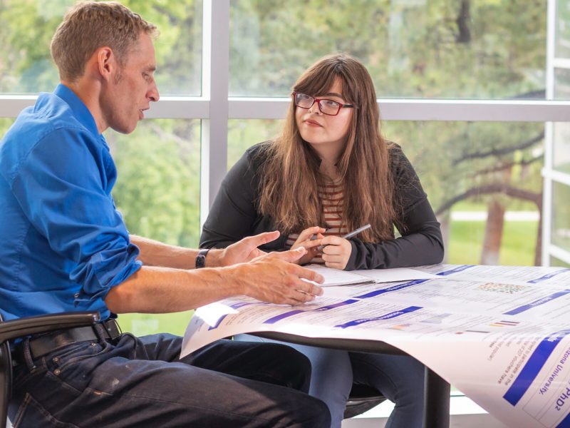 Dirk de Heer talking to a student at a table.