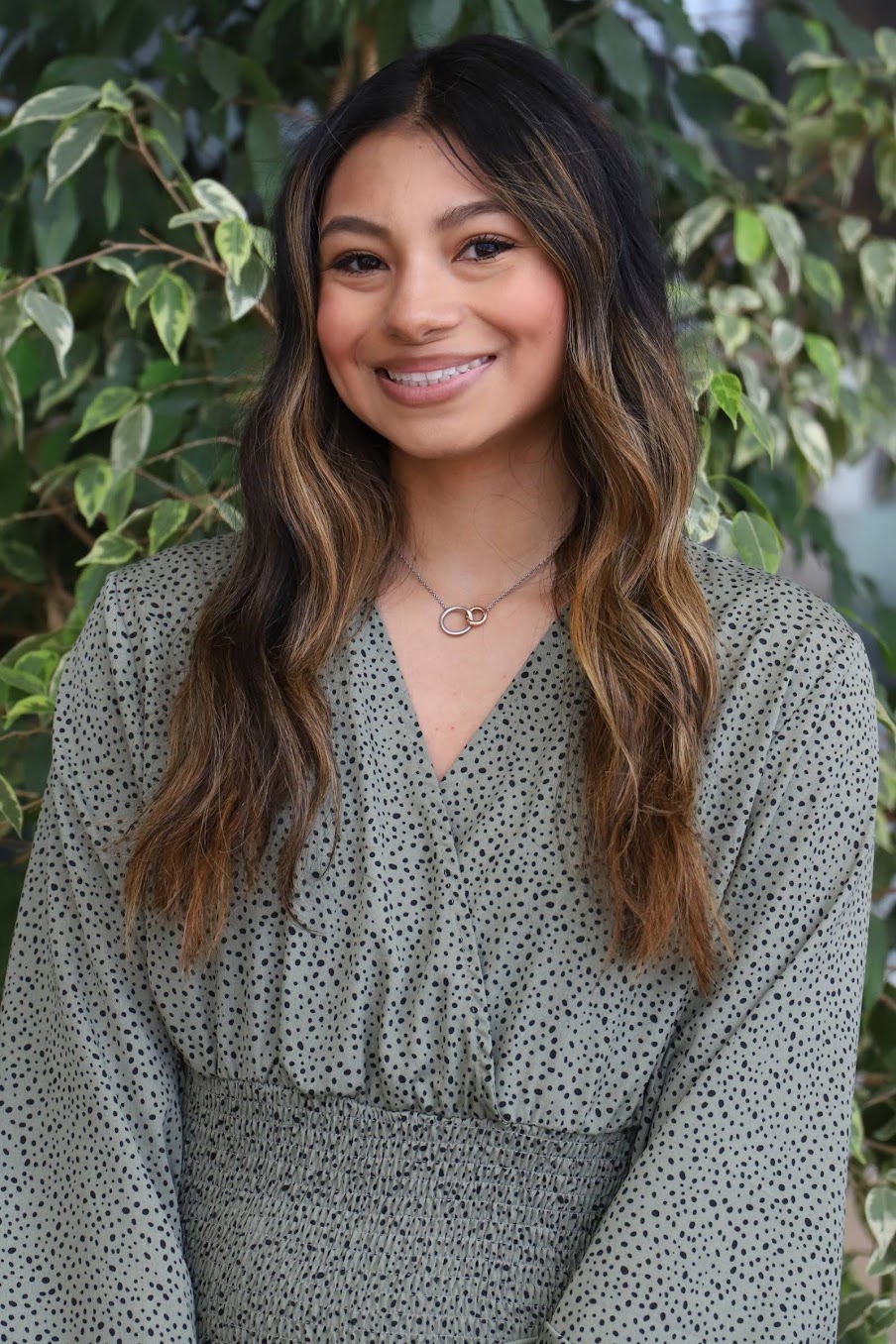 Gabriela Monterroza smiling in front of outdoor leafy vines.