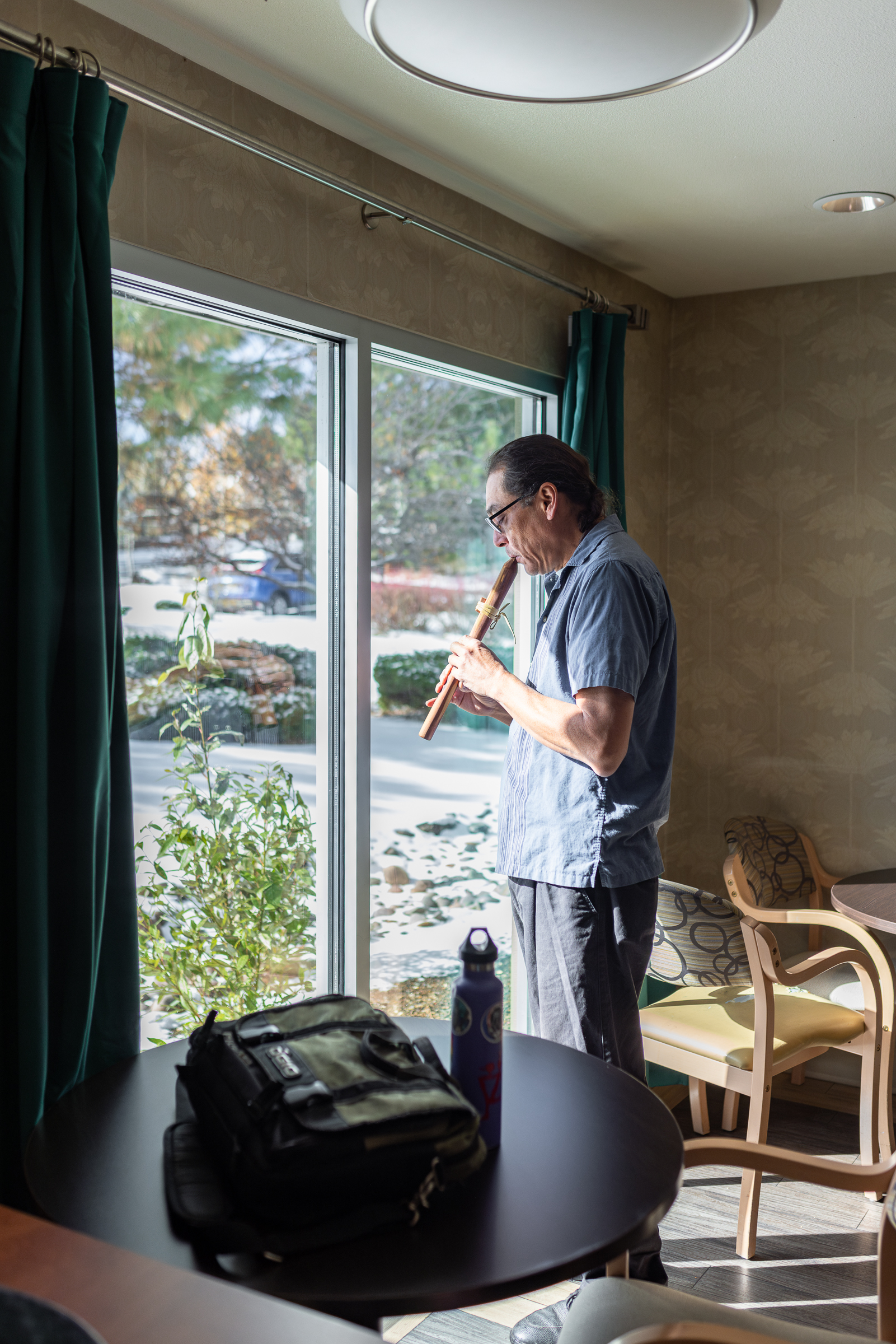 Larry Peterson playing the flute while looking out the bright window at Haven Health.