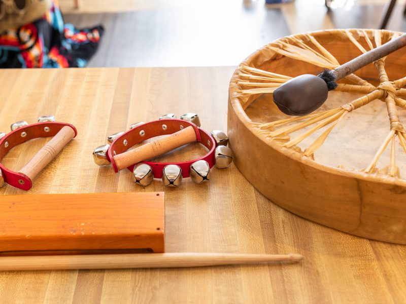 Handheld bells, wood blocks, and personal drums sitting on a table.