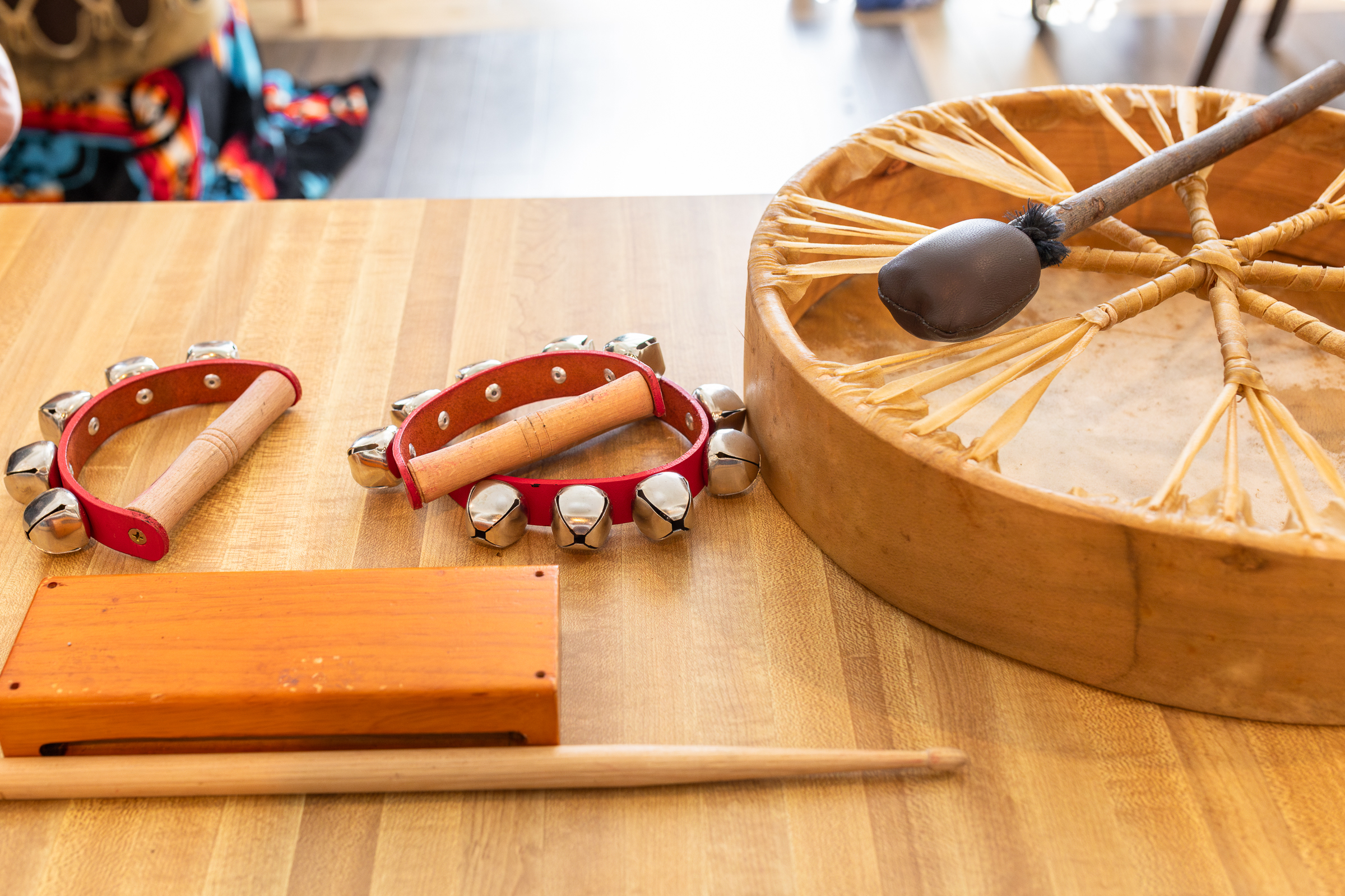 Handheld bells, wood blocks, and personal drums sitting on a table.