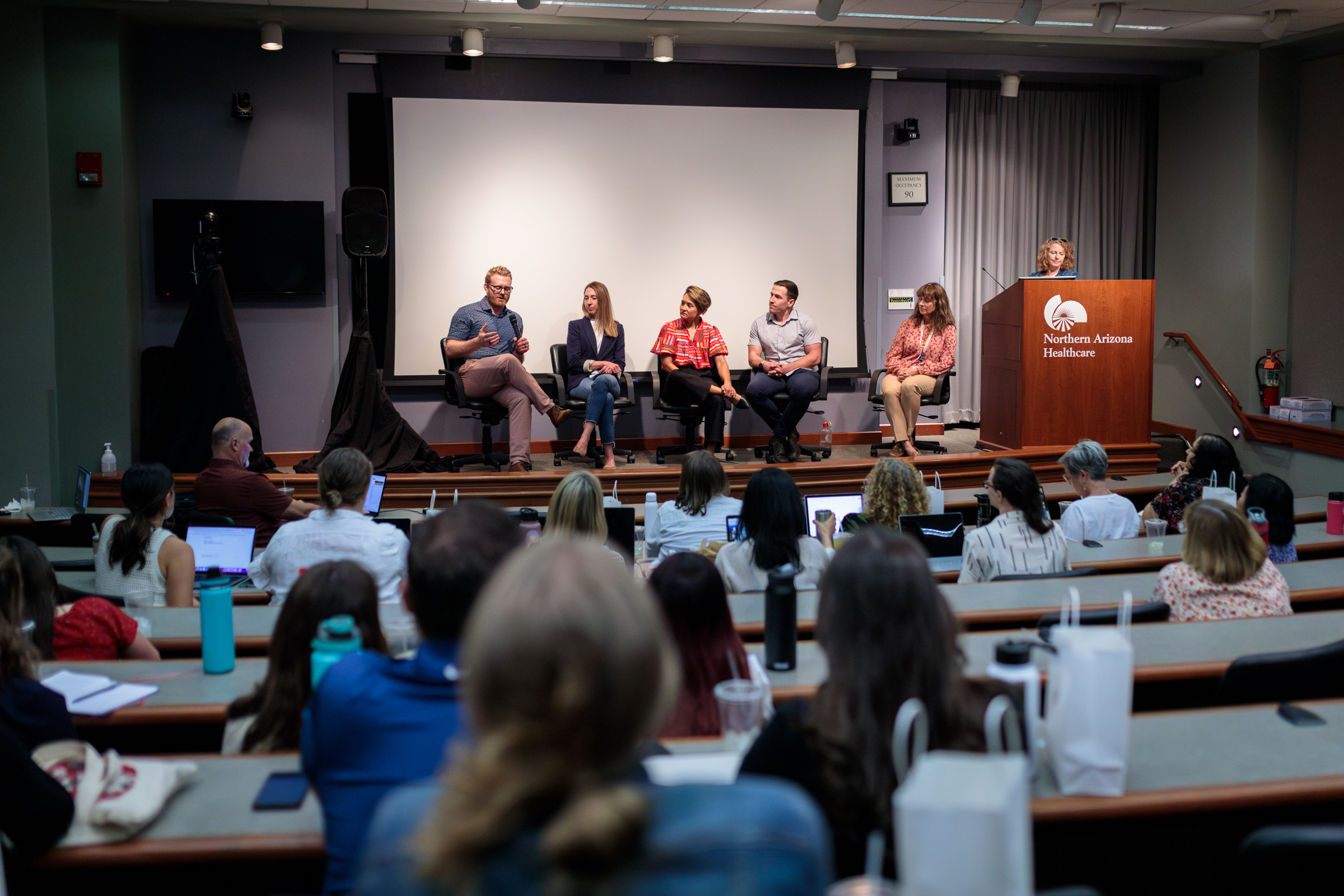 A panel of North Arizona Healthcare speakers sitting in front of a crowded event room.