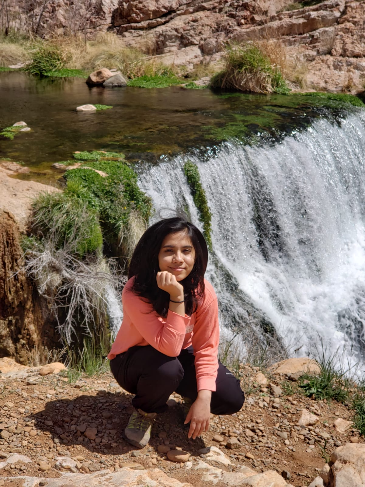 Indrakshi Roy crouched down by a stream with a small waterfall.