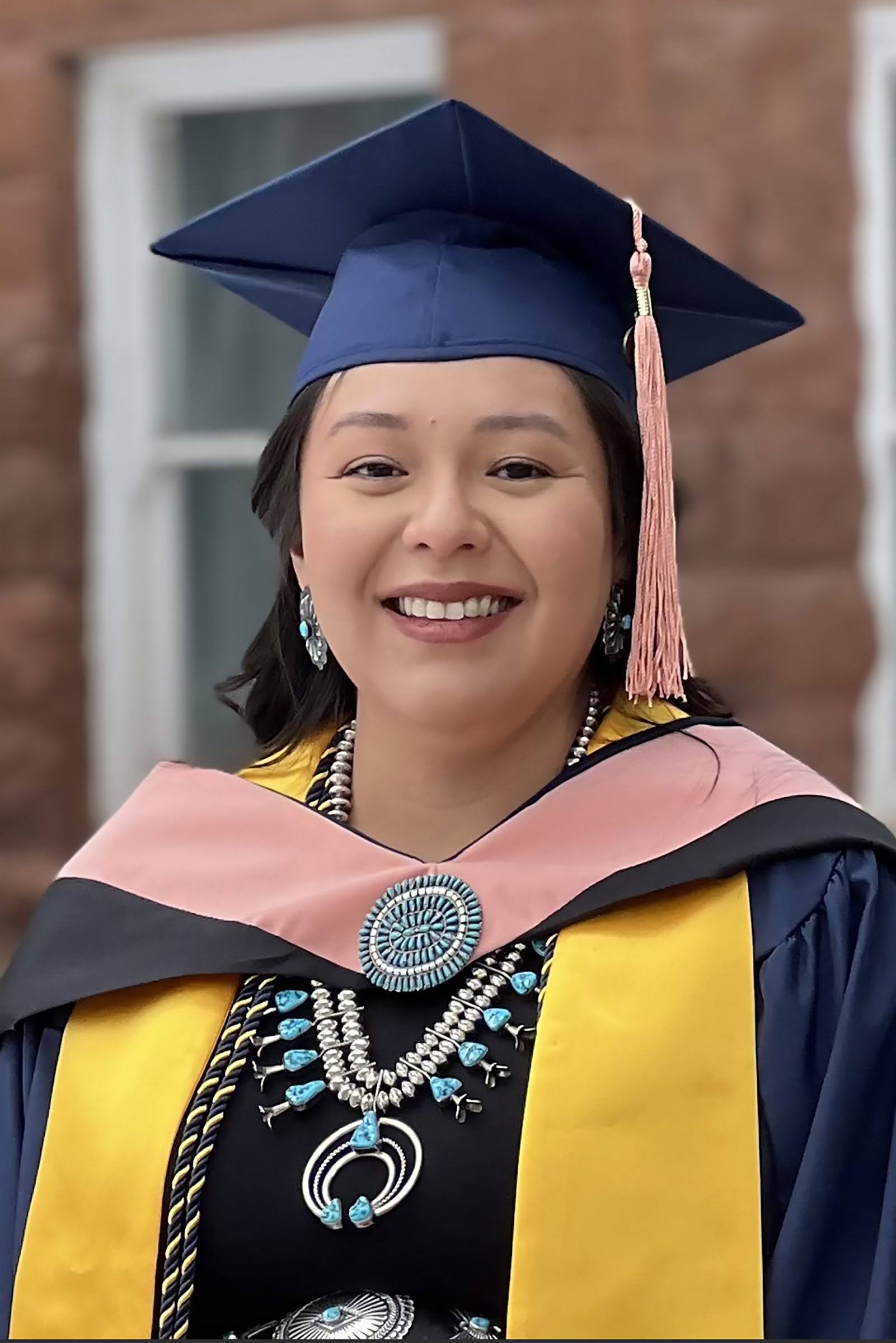 Jayme Biakeddy wearing graduation robe and cap and Native American turquoise jewelry.