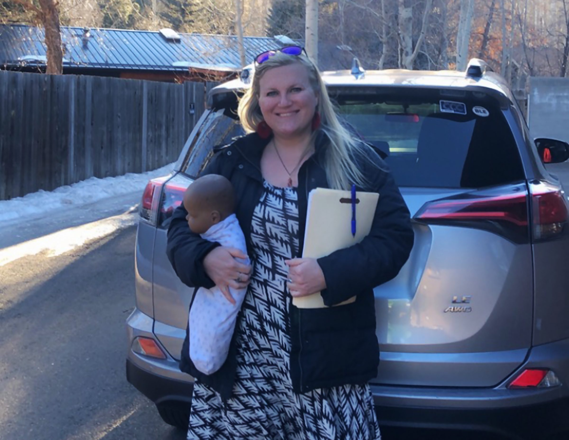 Keri Morrill standing by a vehicle holding a baby and file.