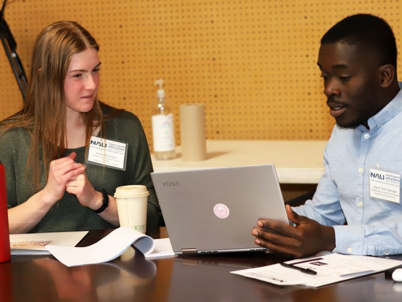 Kofi Mensah sitting at a table with another person working on a laptop.