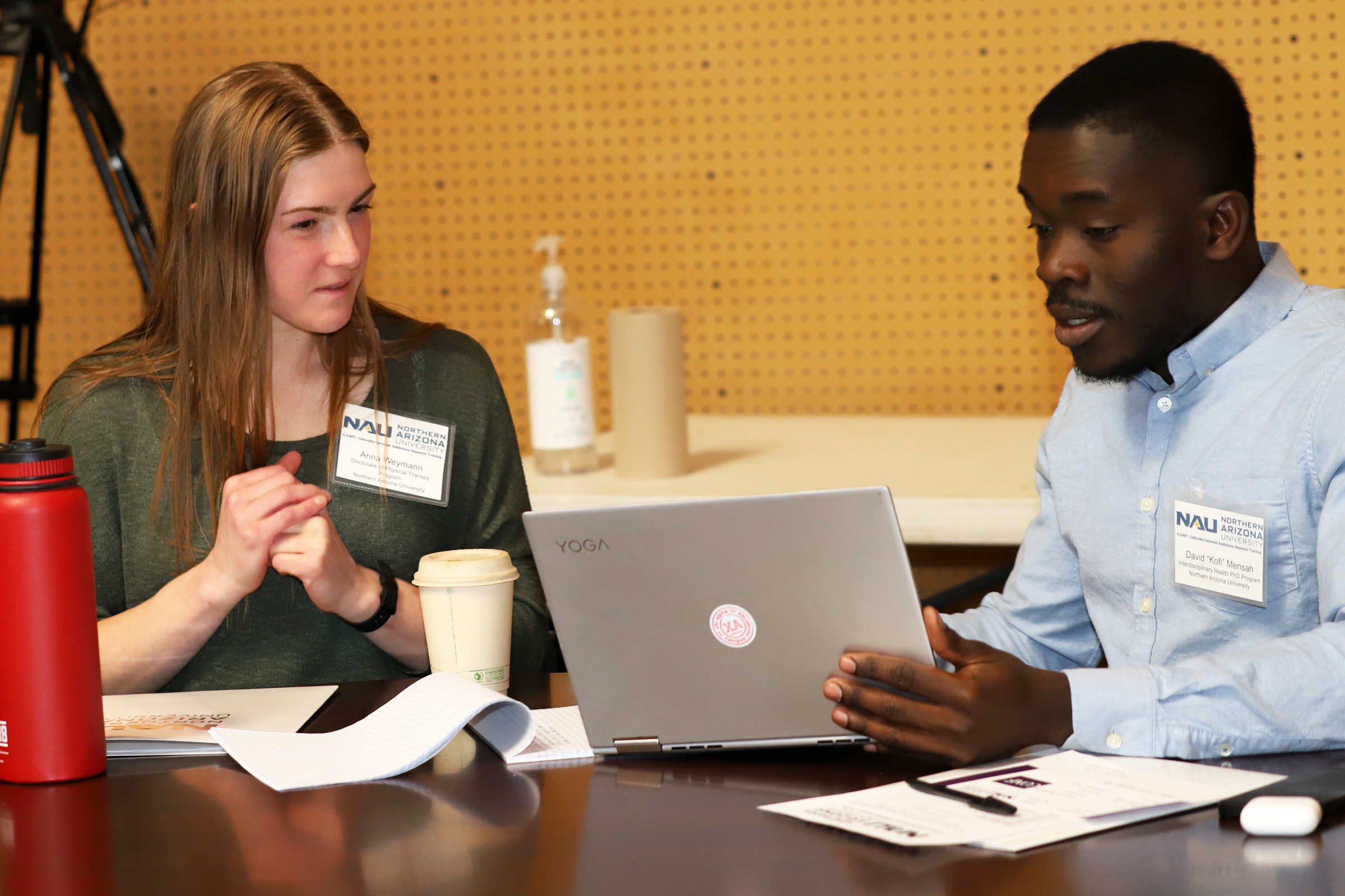 Kofi Mensah sitting at a table with another person working on a laptop.