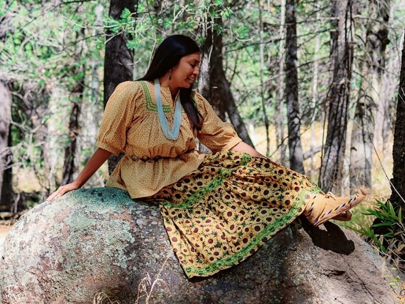 Marissa Tutt wearing a yellow dress while sitting on a rock.