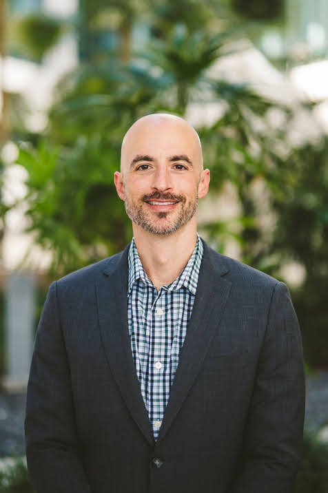 Headshot of Mike Anastario wearing a suit against a green background.