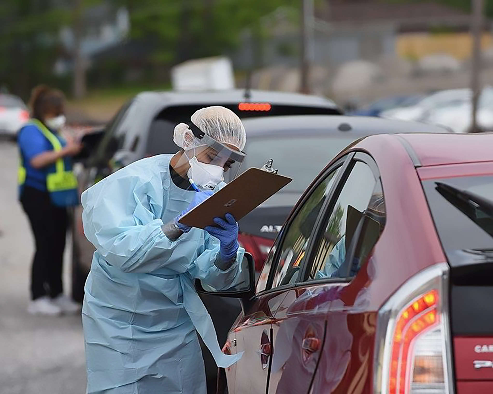 Health care worker in protective wear writing information on a clipboard during COVID-19 pandemic.