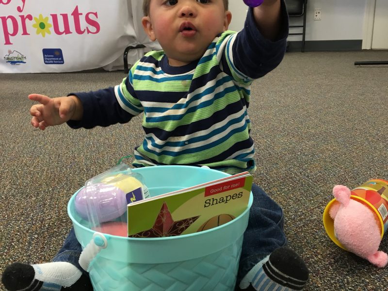 Native American baby playing with toys from a plastic bucket.